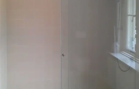 Eine moderne begehbare Dusche mit Glasschiebetüren, beige gefliesten Wänden, einer Regendusche und einer dekorativen Bordüre entlang der Bodenfliesen.